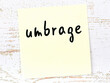 Yellow sticky note on wooden wall with handwritten word umbrage
