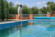 Cleaner of swimming pool. Man cleaning outdoor swimming pool with vacuum tube cleaner in summer. Seasonal preparations. Cleaning systems for swimming pools. Dirty outdoor pool