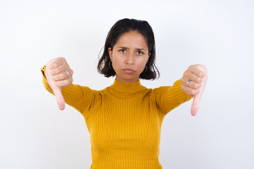 Young hispanic girl with short hair wearing casual yellow sweater isolated over white background being upset showing thumb down with two hands. Dislike concept.