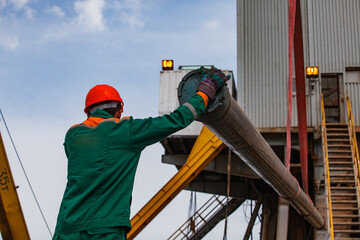 Oil worker with drilling pipe on drilling rig and crane and equipment on oil deposit.