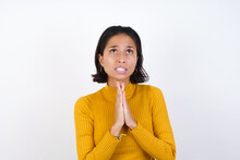Young Hispanic Girl With Short Hair Wearing Casual Yellow Sweater Isolated Over White Background Begging And Praying With Hands Together With Hope Expression On Face Very Emotional And Worried. Asking