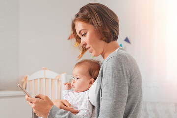 portrait of a mother holding a baby and using a smartphone. side view. the concept of motherhood and
