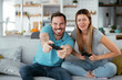 © JustLife - Husband and wife playing video game with joysticks in living room. Loving couple are playing video games at home
