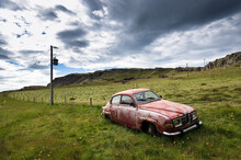 An Old Red Car Rusting In A Green Meadow.