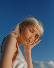 ?lose-up portrait of young blonde with blue eyes with freckles. Portrait of beautiful girl with natural makeup against blue sky