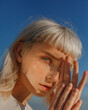 © Tania - ?lose-up portrait of young blonde with blue eyes with freckles. Portrait of beautiful girl with natural makeup against blue sky