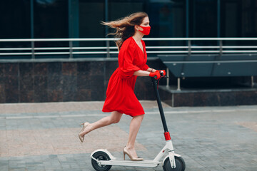 Wall Mural - Young woman with electric scooter in red dress and gloves with face mask at the city. New normal fashion and coronavirus COVID protection concept.