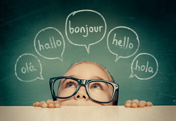 beautiful cute little girl with eyeglasses hiding under table and looking at hello word in french, e