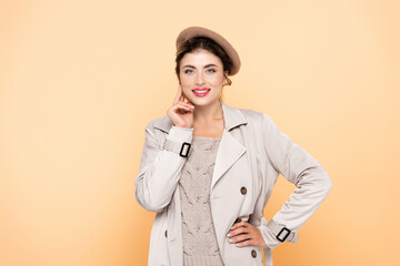 young woman in stylish autumn outfit looking at camera while posing with hand on hip on peach