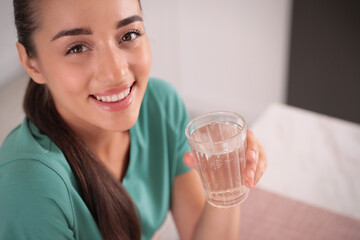 Wall Mural - Young woman holding glass of pure water indoors, closeup