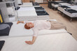 © mad_production - Happy female customer stretching, enjoying lying on orthopedic bed at home goods store