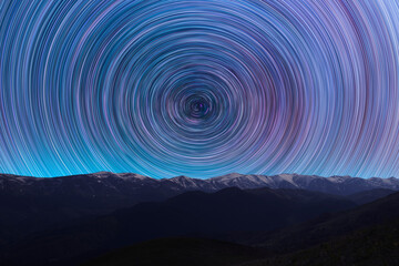 Wall Mural - Long exposure night landscape. Beautiful mountains and. colorful star trails on the sky. Night time lapse photography.