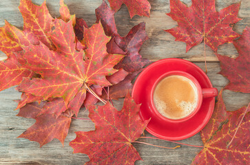 Autumn coffee break. Red cup of coffee and red maple leaves on old wooden background. Top view