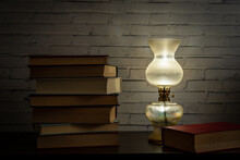The Light Of An Oil Lamp Illuminates Books Placed On A Dark Wooden Surface
