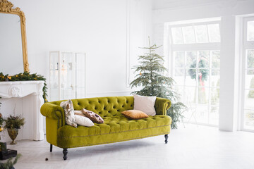 The green velour sofa with pillows in the bright attic room has an artificial fireplace.A spacious living room with white walls and a decorated Christmas tree