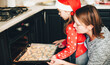© Strelciuc - Christmas preparation by a caucasian family by cooking cakes in the oven wearing red holiday clothes