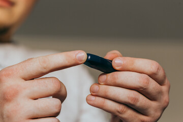 Medicine, diabetes, glycemia, healthcare and people concept - close up of a man's hands using a lancet on his finger to check blood glucose meter with copy space for text