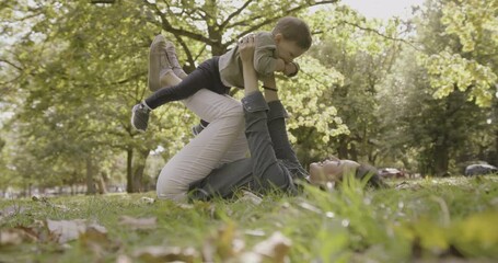 asian female parent lifting toddler up in the air, at park with autumn leafs on sunny day