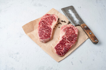 Wall Mural - Two raw fat and juicy beef steaks on craft paper with pepper and a meat cleaver