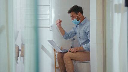 happy businessman working on laptop wearing mask sit on the toilet at home restroom bearded funny wc