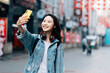 © MaaHoo Studio/Stocksy - Young asian woman traveling in a city downtown and taking selfie with cell phone