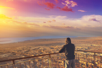 Wall Mural - Young man standing on a viewpoint on the mount (Masada) and gazing sunrise over the Dead Sea. Dead sea region, Masada, Israel