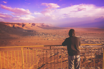 Wall Mural - Young man standing on a viewpoint on the mount (Masada) and gazing sunrise in the desert. The man looking at the valley. Dead sea region, Masada, Israel