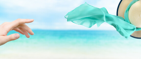 Female straw hat with silk scarf flying away on the wind on sea background.