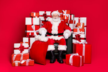 Wall Mural - Full length body size view of his he handsome fat overweight cheerful Santa Saint Nicholas sitting in chair pile stack giftboxes isolated bright vivid shine vibrant red color background