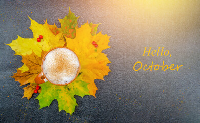 Wall Mural - Cup of cappuccino coffee stands on maple leaves on a dark background with the words Hello October. Concept of autumn mood flat lay. Beautiful autumn background