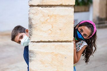 Two funny kids with face masks behind a column