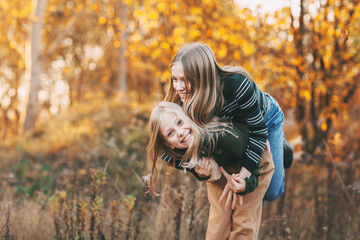 two happy little girls sisters laughing, having fun and playing in the fall in nature outdoors in th