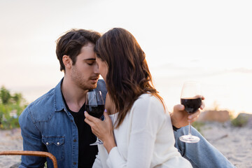 Wall Mural - Young couple with glasses of wine kissing on beach at sunset