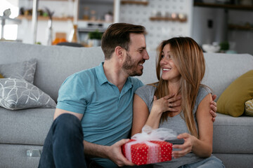 Husband surprising his wife with a gift. Young man giving gift box to his wife.