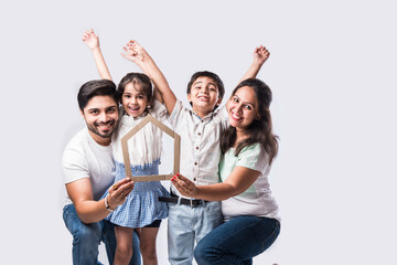 Real Estate Concept - Indian happy and young family of Four holding 3D paper model of home.