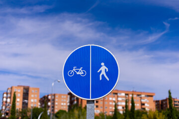 Low angle view of a sign indicating two lanes, one for bicycles and one for people, with some buildings and a blue sky in the background