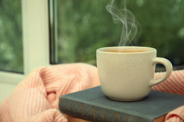 Poster - Cup of hot coffee, books and warm sweater on window sill indoors. Space for text