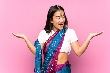 Wall Mural - Young Indian woman with sari over isolated background holding copyspace with two hands