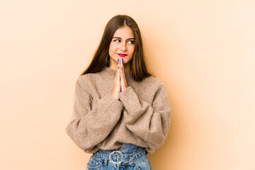 Young caucasian woman isolated en beige background praying, showing devotion, religious person looking for divine inspiration.