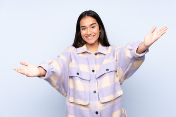 Wall Mural - Young Indian woman isolated on blue background presenting and inviting to come with hand