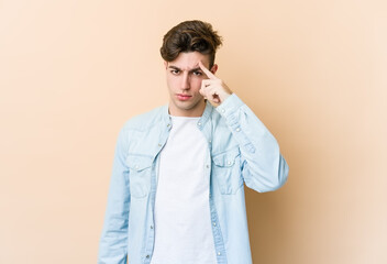 Wall Mural - Young caucasian man isolated on beige background pointing temple with finger, thinking, focused on a task.