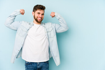 Wall Mural - Young caucasian man isolated on blue background showing strength gesture with arms, symbol of feminine power