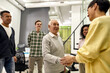 © Svitlana - Cheerful young team greeting new employee hired worker in the modern office, Aged man or senior intern shaking hands with his colleagues
