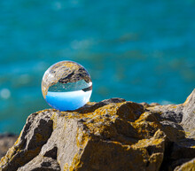 Photography Crystal Photo Ball Showing Upside Down Reflection Of Sky Beach And Waves Balanced On Rocks On Sandy Beach.