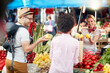 © luckybusiness - Seller woman offers fresh and organic vegetables at the green market or farmers market stall.  Young buyers choose and buy products for healthy food in grocery. All for diet healthy eating, lifestyle.