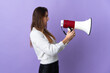 © luismolinero - Young Ireland woman isolated on purple background shouting through a megaphone to announce something in lateral position