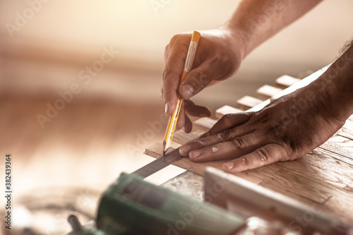 Fotomural Carpenter on work uses a pencil to sign measurement when installing pre-finished parquet