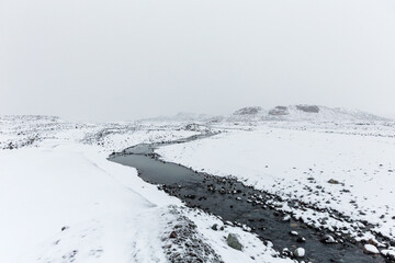 Canvas Print - Snow covered landscape and blue water stream in Icelandic highlands