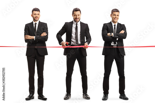 Cuadros en Lienzo Full length portrait of a three businessmen cutting a red ribbon tape at an even
