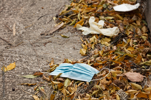 A mask and gloves were used for medical protection lost on the ground. Disposable mask lying on the street. Incorrectly discarding the used face mask, on plant leaves in autumn